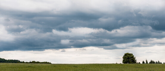 Beautiful view of the landscape of Bohemian Switzerland. The photo shows a meadow, trees and especially the sky, which stands out in the photo. The sky is cloudy with dark clouds.
