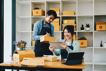 Asian couple doing online business together at home. Helping to pack products into cardboard boxes....