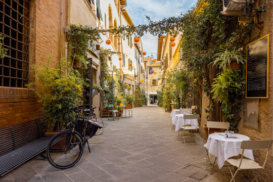 Fototapeta Beautifully landscaped narrow street with restaurant tables in the old town of Grosseto, in Maremma region of Italy. Cozy city view of the old Italian town