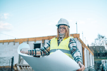 A technical engineer 30s woman in construction helmet with document analyzes an unfinished construction project.