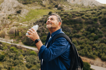 Mature man drinking some water on a mountaintop