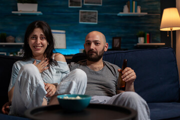 POV of girlfriend and boyfriend watching movie on TV channel to have fun with leisure activity. Cheerful couple enjoying broadcast film on television program, having beer and popcorn.