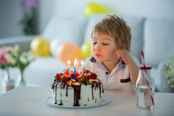 Four years old blond child, preschool boy, celebrating birthday at home with homemade cake