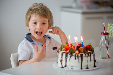 Four years old blond child, preschool boy, celebrating birthday at home with homemade cake