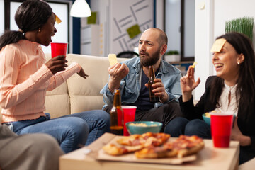 Office colleagues playing guess who charades game at party celebration with alcoholic drinks and snacks. Cheerful people using sticky notes to have fun and do leisure activity after work.