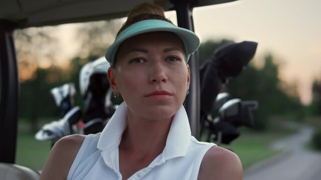 Golf woman looking camera at nature. Beautiful golfer sit in buggy car on course