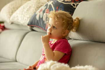 Fototapeta premium Cute little blond toddler girl, sitting in front of the TV with popcorn, watching movie with her pet dog