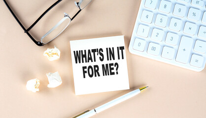 WHAT'S IN IT FORME text on sticky with pen ,calculator and glasses on beige background