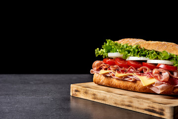 Submarine sandwich with ham, cheese, lettuce, tomatoes,onion, mortadella and sausage on black background. Copy space