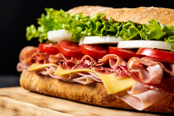 Submarine sandwich with ham, cheese, lettuce, tomatoes,onion, mortadella and sausage on black background