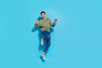 Full body photo of hooray young brunet guy jump hold tablet thumb up wear shirt jeans sneakers...