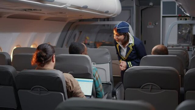 Female stewardess asking passengers about airline services and flying, boarding travellers on airplane seats. Travelling with international airways, chatting on aeroplane jet and going on vacation.