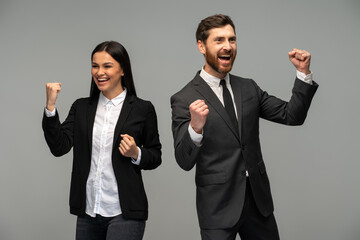 Handsome businessman and gorgeous businesswoman rejoicing and laughing while posing over grey background