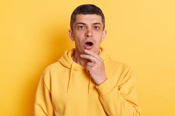 Surprised amazed man wearing casual style hoodie posing isolated over yellow background, looking at camera with big eyes and open mouth, shocked by news.