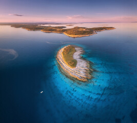 Aerial view of small island, Kamenjak cape, Adriatic sea, Croatia at sunset in summer. Beautiful landscape with sea coast, mountains, clear water, purple sky at twilight. Top view from drone. Panorama