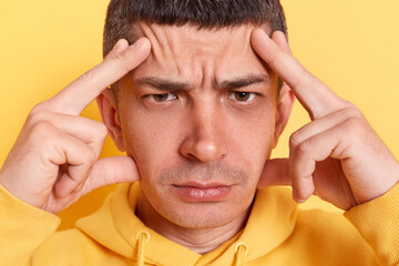 Depressed ill man wearing casual style hoodie posing isolated over yellow background, frowning and...