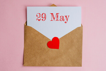 Kraft envelope with a white sheet of paper and a date 29 may, with a red heart. Flat lay on pink...