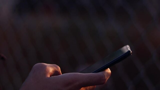A man using telephone near the iron fence During the sunset near the ground.