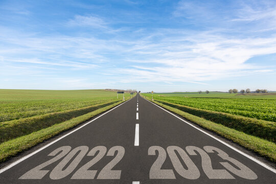 Empty road surrounded by green fields and the years 2022-2023 written	
