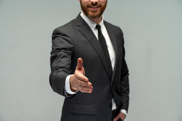 Close up view of the male businessman in a suit stretching hand and shows a palm up gesture on a grey background. Concept of request, handshake