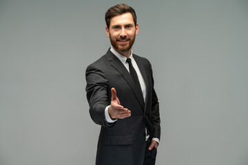Male businessman in a suit stretching hand and shows a palm up gesture on a grey background....