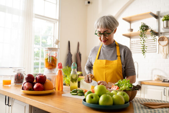 senior female preparing infused water,healthy vegetarian with fruits and vegetables in kitchen room at home.Old cheerful people taking care about nutrition,Health care,vegan concept.