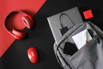 Urban gray backpack with laptop, notepad, pen, phone and external ssd drive on a red and black...