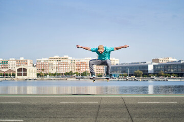 a man doing an ollie with his skateboard on an asphalt road next to the harbor