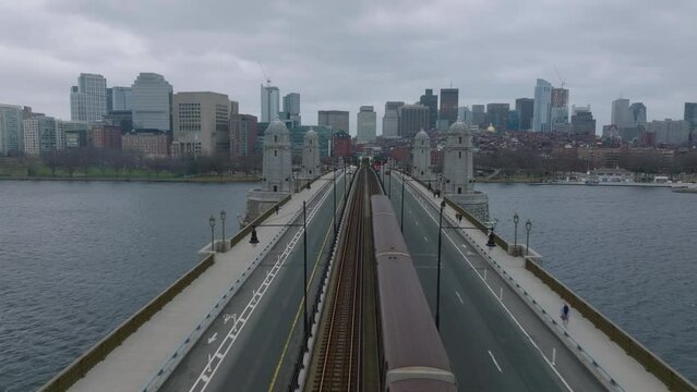 Forwards fly above Longfellow Bridge with train and cars. Cityscape with downtown buildings against cloudy sky. Boston, USA