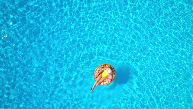 Aerial view of a woman in yellow swimsuit lying on a donut in the pool