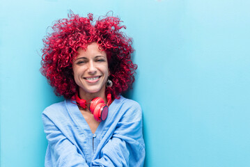 portrait of a smiling young latin woman with a red afro hair in blue background looking at the...
