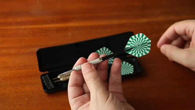 Hands take darts out of the box and insert plastic plumage on a brown wooden table