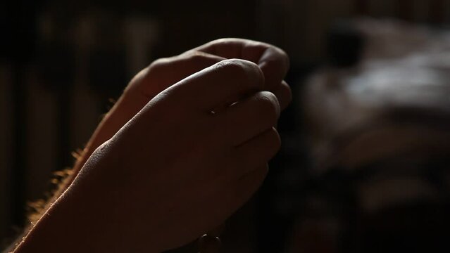 man sorting with two hands a round wooden rosary on a black background close-up. A dim light falls from above