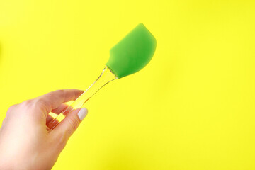 Womans hand holding  silicone green spatula with plastic handle on color background- Image