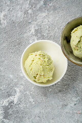 Two scoops of pistachio ice cream in bowls on light surface