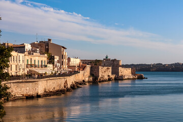 Naklejka premium Panoramic view on the waterfront of the city of Syracuse, Sicily, Italy, Europe EU. Soft light shining on the residential houses at the Mediterranean seaside. Walking along the coastline