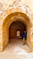 Tourist man leaning agains wall of vaults of the Castello Maniace. Interior of ancient citadel fortress Maniace Castle on island of Ortygia in Syracuse, Sicily, Italy, Europe EU. UNESCO Site. Tunnel