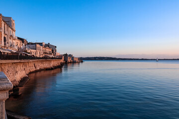 Panoramic sunrise view on the waterfront of the city of  Syracuse, Sicily, Italy, Europe EU. Soft light shining on the residential houses at the Mediterranean seaside. Walking along the coastline