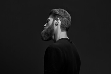 Black and white portrait of bearded stylish man turning back from camera isolated on black...