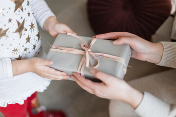 Woman's hands give a gift to a girl. Mom gives a Christmas present to her daughter