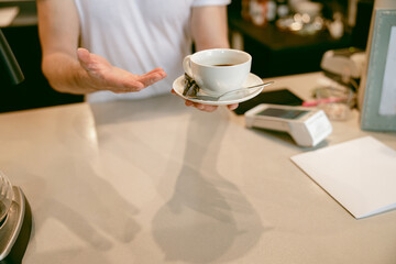 White cup of coffee in male hands of barista. Serving, giving drink to camera. Cafe work. Close up.