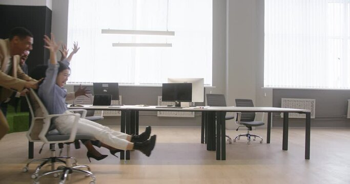 Men push women on chairs against empty table with computers