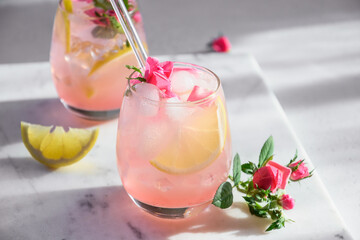 Freshness pink lemonade with rose gin garnish lemon in sunny shadow on white background. Close up.