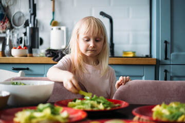 Obraz na płótnie Canvas Little blonde girl is helping to prepare dinner in the kitchen.