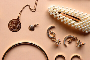 Various gold jewelry and pearl hair clips on peach colored background. Flat lay.