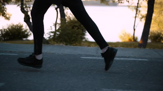 Side tracking shot with legs of a man running early in the morning on the seafront