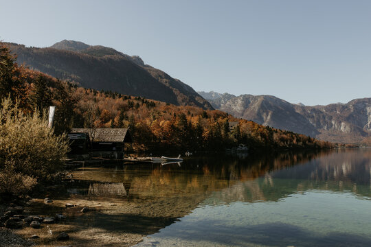 Stunning autumn landscape by lake Bohinj in Slovenia. Lakeside mountains and cristal clear water. Boathouse, fall colors, sunshine, nobody. Copy space. Reflection on the water. Idyllic panorama.