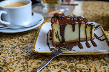 cheesecake covered with chocolate and a cup of coffee on a table in a cafe.