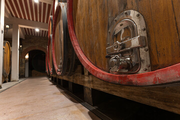 Fototapeta na wymiar The ambiance of the traditional wine cellar, aging red wine barrels, wooden casks in rows in the winery underground storage room
