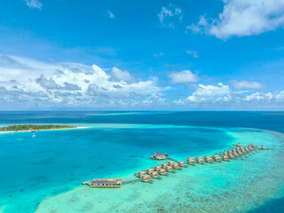 Naklejka na ściany i meble Aerial view of Maldives island, luxury water villas resort and wooden pier. Beautiful sky and ocean lagoon beach background. Summer vacation holiday and travel concept. Paradise aerial landscape pano